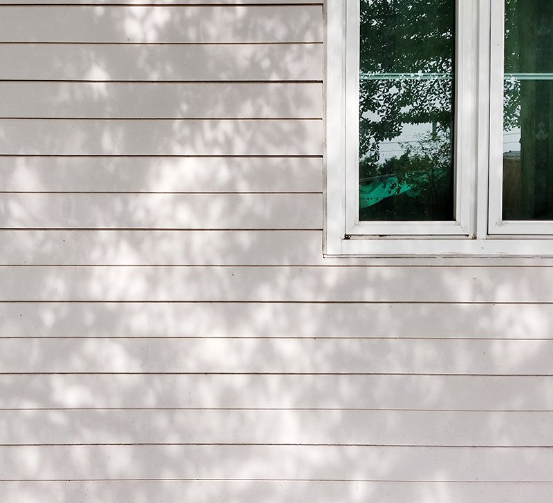 White Alside vinyl siding on a residential exterior with dappled light